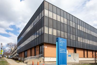 Large modern office building under blue sky and clouds, with a directory sign out front. POV is facing the building corner.